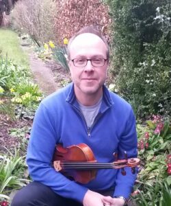 Byron Parish sitting in his garden holding his violin